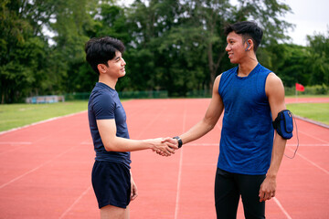 Two Asian male athletes shaking hands on an outdoor running track, symbolizing teamwork, sportsmanship, and respect after workout or competition. Concept of fitness partnership and motivation