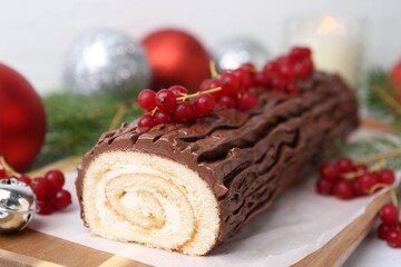 Delicious Yule log (traditional Christmas cake) with redcurrant and decor on table, closeup