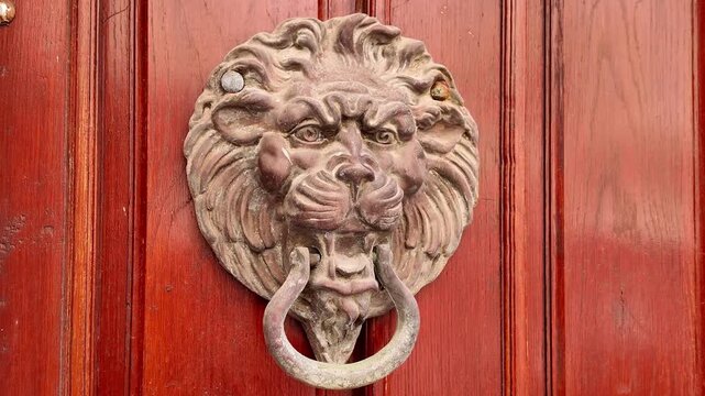 Detailed close-up view of an antique lion head door knocker.
The vintage metal ornament with a ring is mounted on a classic red wooden door