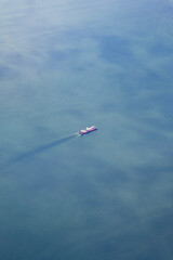 Aerial view of a cargo ship sailing across calm blue ocean water leaving a faint trail