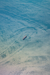 Aerial view of a small cargo ship sailing through calm turquoise ocean water, leaving swirling patterns behind