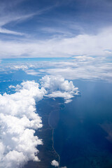 Aerial view of coastline and ocean beneath white clouds and bright blue sky from an airplane