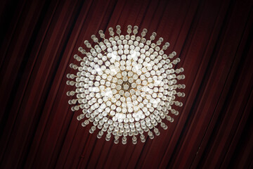 Elegant crystal chandelier viewed from below against a dark red ceiling, creating a symmetrical...