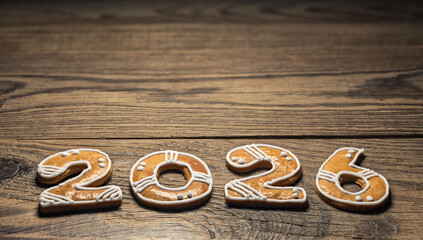 Closeup of gingerbread 2026 number for New year greetings on vintage background. Beautiful Xmas still life with golden baked sweets in numerals shape decorated by white frosting on brown natural wood.