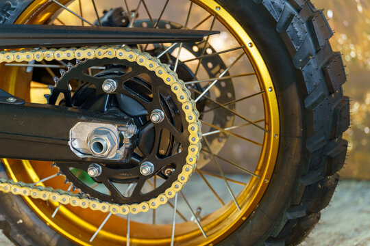 Close-up view of a motorcycle wheel with a gold chain and black tire in sunlight