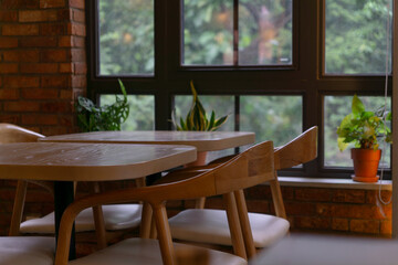 A cozy indoor dining area with wooden tables and chairs, large windows letting in natural light, and potted plants adding a touch of greenery.