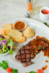 Grilled steak with sides and sauces on a plate. The dish is presented on a plate with various garnishes