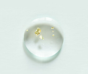 Transparent water droplet with floating gold flakes on white background.