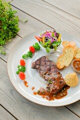A gourmet steak dish presented on a plate, featuring a grilled steak with pepper sauce, garlic bread, salad, and tomato garnish