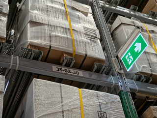 A low-angle view of tall metal warehouse shelving stacked high with shrink-wrapped boxes, featuring...