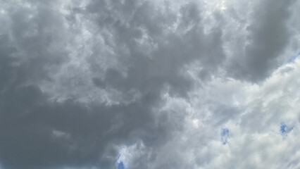 A full-frame view of a dynamic, dramatic sky dominated by dense, dark gray storm clouds with hints...