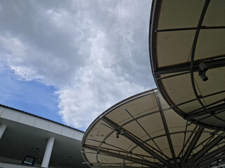 Low-angle view of two large curved fabric canopies with radial metal frames beside a modern building under a partly blue, cloudy sky.