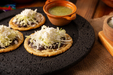 Sopes. Mexican typical food prepared with flattened fried corn dough covered with refried beans, green or red sauce, lettuce, cheese, onion and sour cream. Mexican antojitos.
