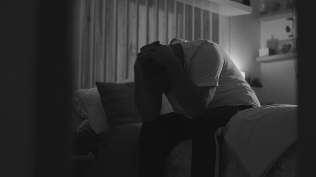 Middle-aged man sitting on bed at night with head in hands, overcome by guilt and emotional pain, expressing deep sorrow and regret in quiet solitude
