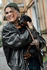 Woman with a dachshund dog in a leather jacket smiling outdoors