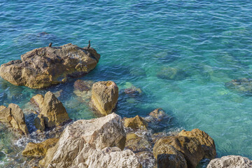 Rocky shoreline with clear turquoise water gently lapping against stones, creating a serene coastal landscape ideal for relaxation and nature appreciation