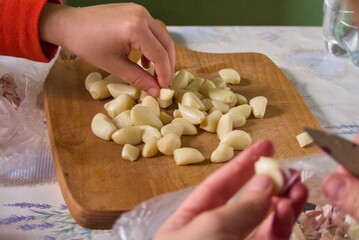 Preparing fresh garlic cloves - Close-up of hands peeling and preparing numerous fresh garlic cloves on a wooden cutting board