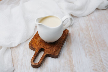 White jug filled with organic milk on wood board with white cloth background