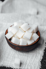 Cubes of white sugar in a wooden bowl on a textured cloth background