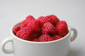 Raspberries in white bowl on light surface for organic food or vegan diet concept