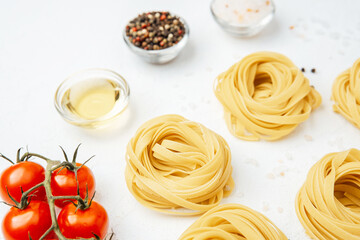 Raw tagliatelle pasta nests with tomatoes and spices on white background