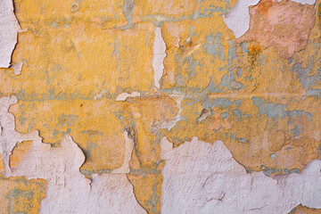 Rough textured aged wall with peeling paint showing yellow and pink layers, weathered surface.