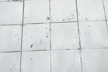 Naklejka premium Old white tiles surface, weathered and chipped, showing textured grid pattern close up.