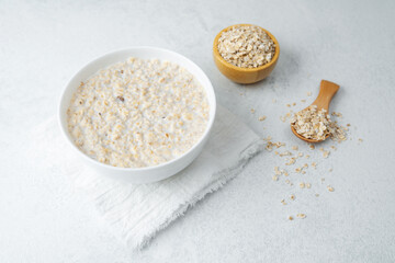 Oatmeal porridge with raw oats and wooden spoon on light background