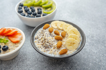 Three oatmeal bowls with kiwi banana and strawberry on gray background