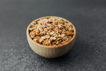 Granola in round wooden bowl on dark background