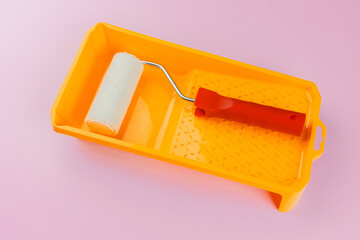 Paint roller in yellow tray on pink background for painting gear and DIY home concept