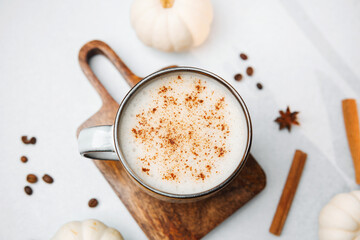 Warm coffee drink with cinnamon and foam in a mug, surrounded by pumpkins and spices.