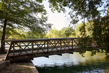 Fototapeta premium HOUSTON, TEXAS - OCTOBER 18th 2025: Serene park landscape with a calm waterway, arched bridge, lush green grass, and vibrant autumn trees, perfect natural backdrop for portrait photography.