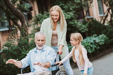 Heartwarming family care moment as grandpa in a wheelchair is guided by his daughter and granddaughter in a sunny park