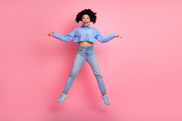 Excited young woman jumping with joy in casual fashion on pink background symbolizing freedom and happiness