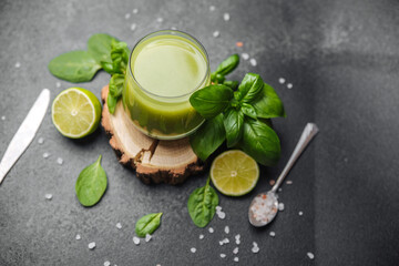 Fresh green juice with basil, lime, and spinach on stone surface with cutlery and salt