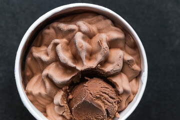 Frozen chocolate ice cream swirl with scoop inside paper cup on dark background