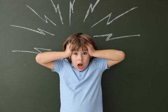 Back to school. Emotional boy near chalkboard with drawn lightning bolts indoors - Powered by Adobe