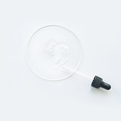 Clear cosmetics dropper with serum on white surface and transparent petri dish.