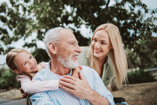 Funny family moment in the park as grandpa in a wheelchair shares a warm smile with daughter and wife during a sunny day