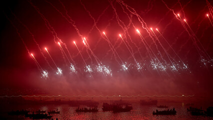 A vibrant display of red fireworks shines above boats floating on the Ganga River during Dev Deepawali in Varanasi.