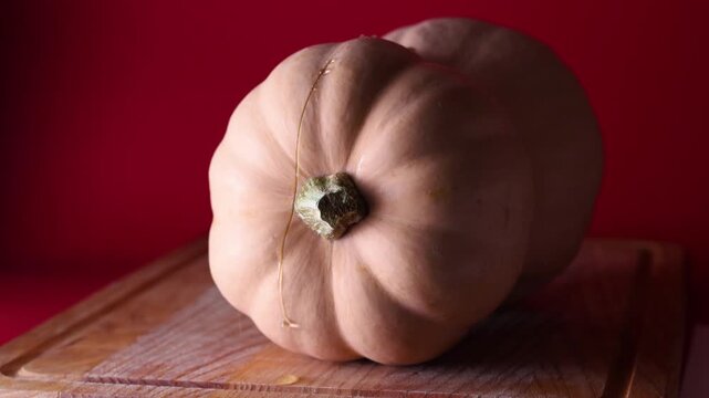 Static close-up shot of a butternut squash partially cut in half from the stem side, showing transparent juice drops slowly running down the fresh cut. The squash rests on a wooden cutting board