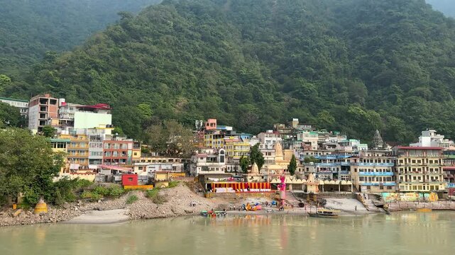 Panoramic view of Rishikesh city with colorful buildings along the banks of the Ganges river and green hills, India