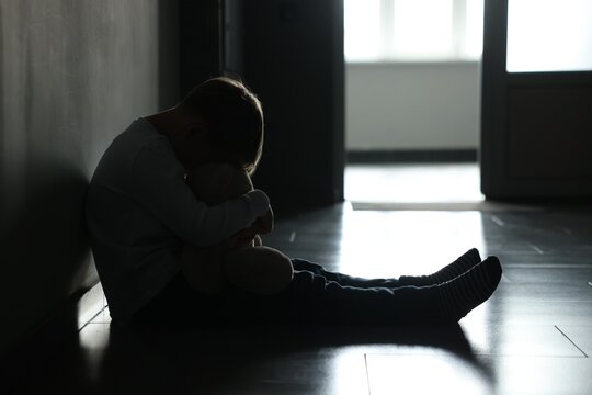 Upset little boy with toy bear near wall indoors
