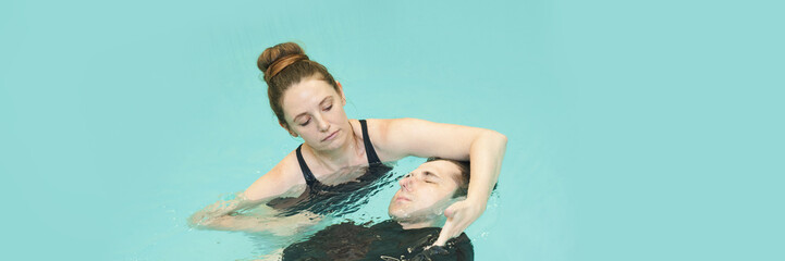Female instructor teaching male adult in pool therapy session for rehabilitation and relaxation in calm aquatic environment.