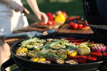 Vegetarian barbeque. Woman cutting products at table outdoors, focus on grill with cooked vegetables