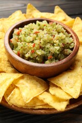 Tasty salsa in bowl and nachos on wooden table, closeup