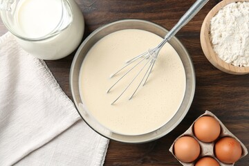 Liquid dough in bowl, whisk and ingredients on wooden table, flat lay