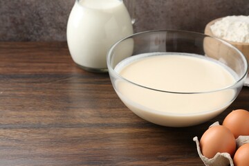 Liquid dough in bowl and ingredients on wooden table, closeup. Space for text