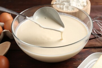 Taking liquid dough from bowl with ladle on wooden table, closeup